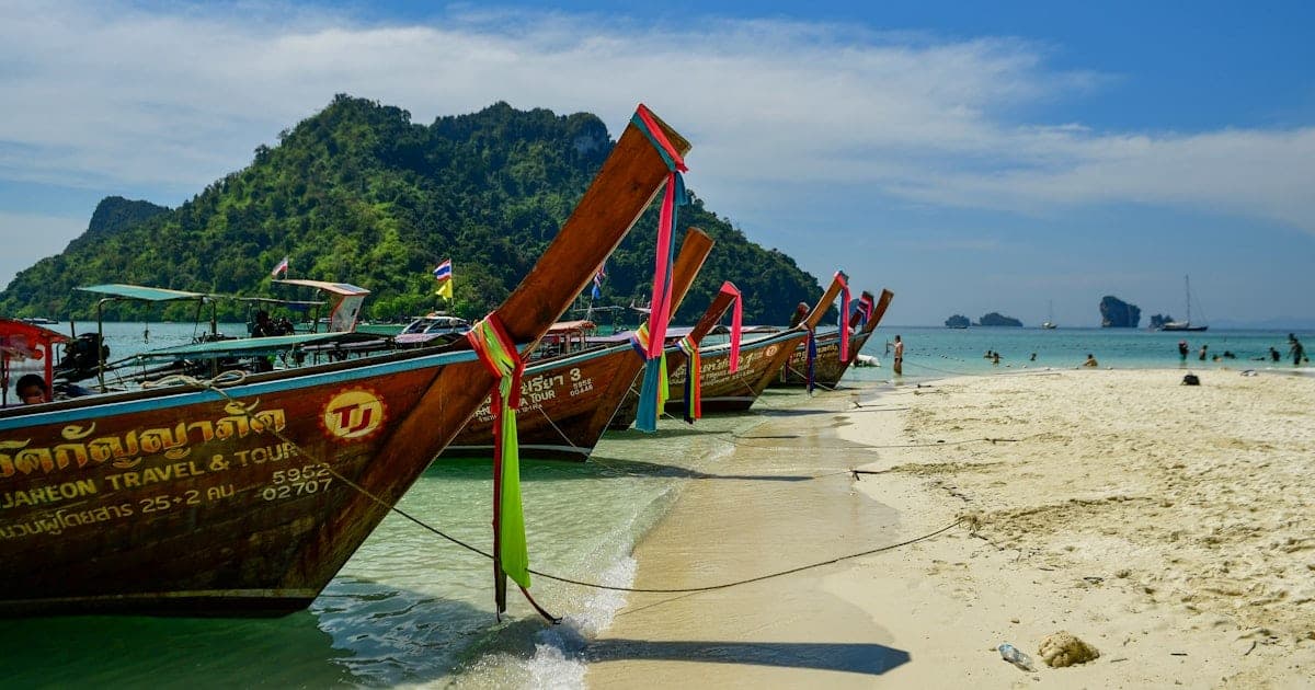 A backpacker watching a longtail boat cross turquoise water between limestone islands in Southeast Asia
